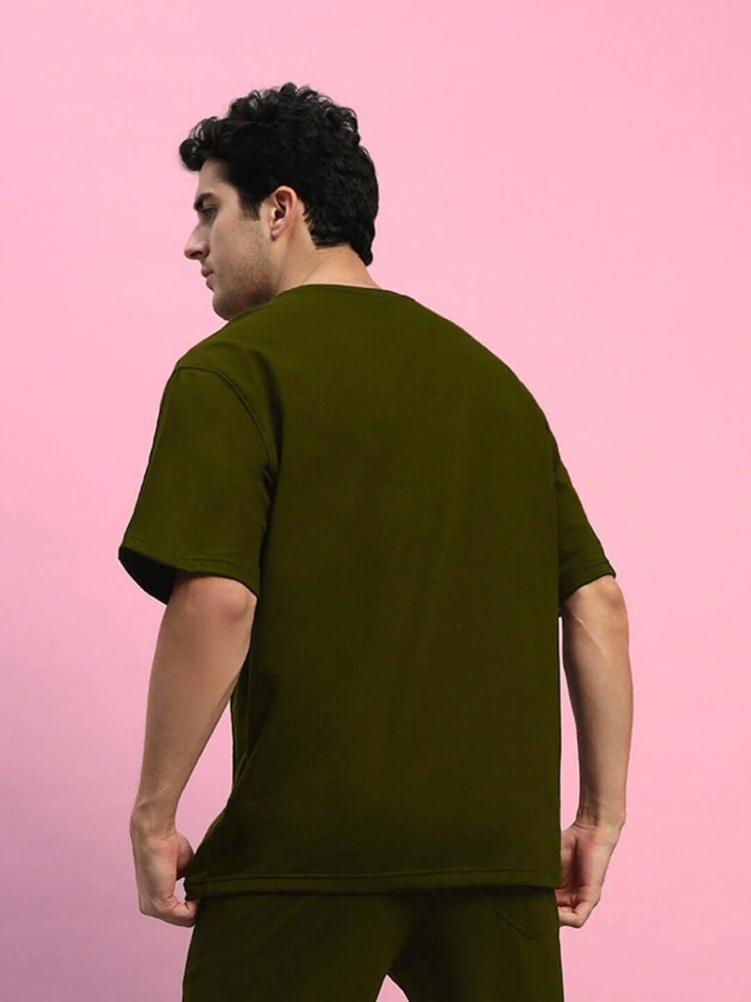 Man wearing an olive green oversized T-shirt, showcasing premium heavy gauge fabric, against a pink background.