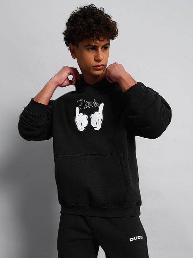 Model wearing WEARDUDS SUPREME FLEECE HOODIE BLACK, hands pulling the hood strings, showing stylish fleece design.