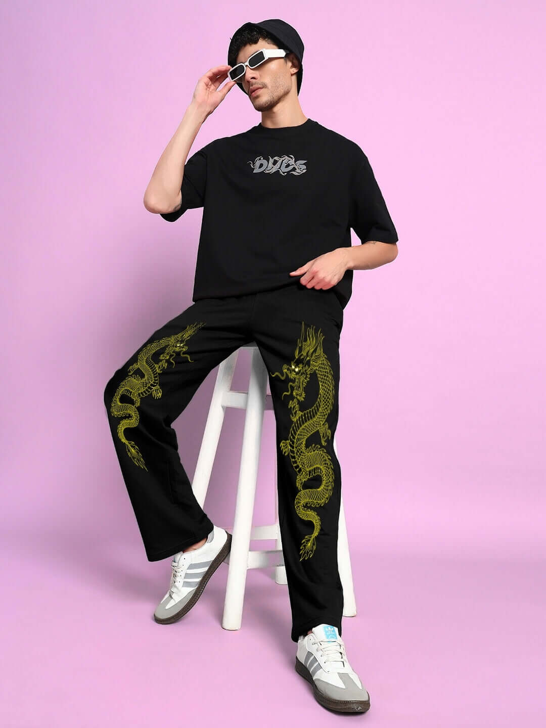 Man wearing SUPREME DRAGON PRINTED RELAXED FIT JOGGER BLACK, sitting on stool, showcasing bold dragon print design.