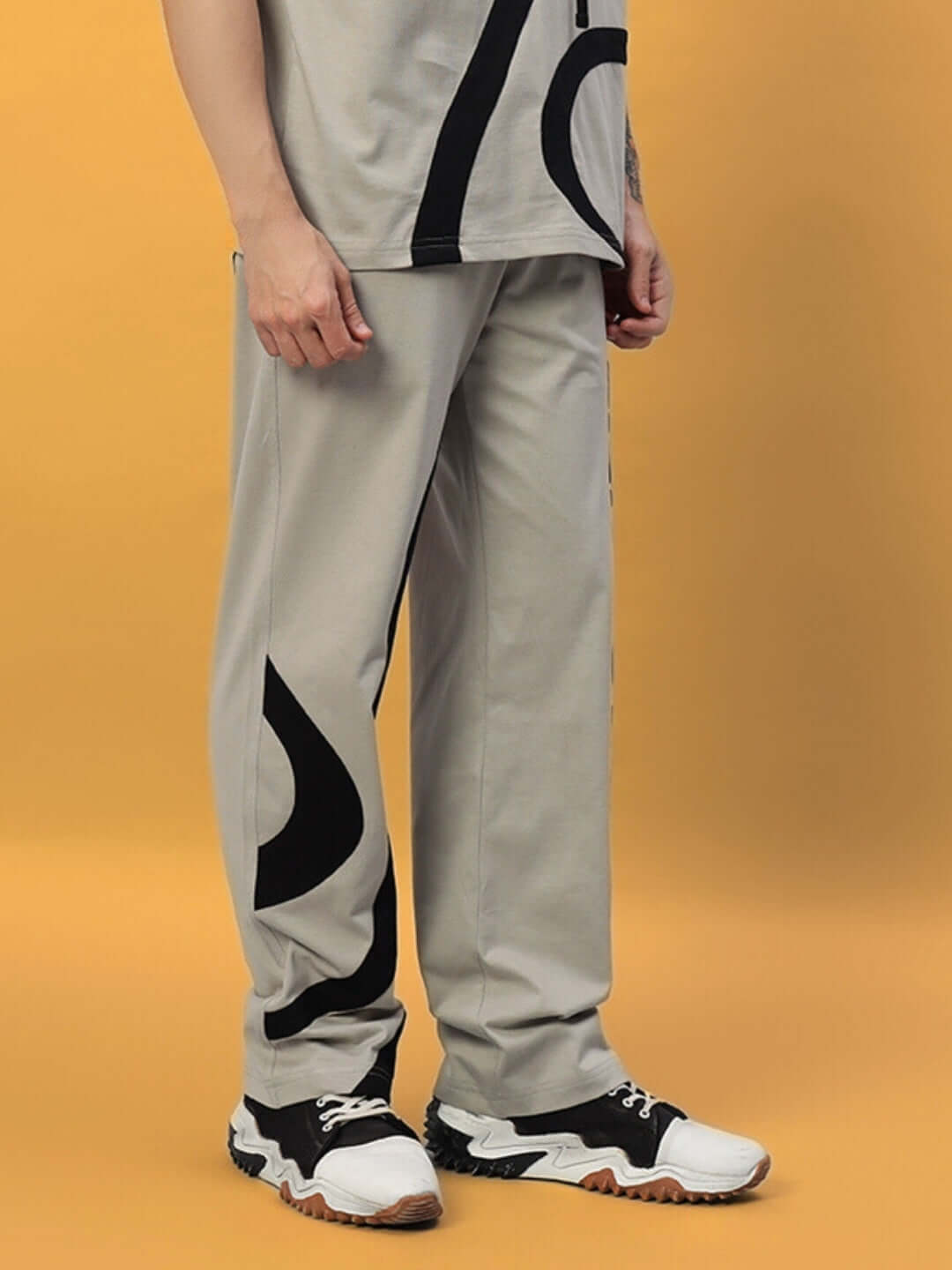 Man wearing grey surfing jogger pants with black abstract design, showcasing casual and comfortable style on a mustard background.