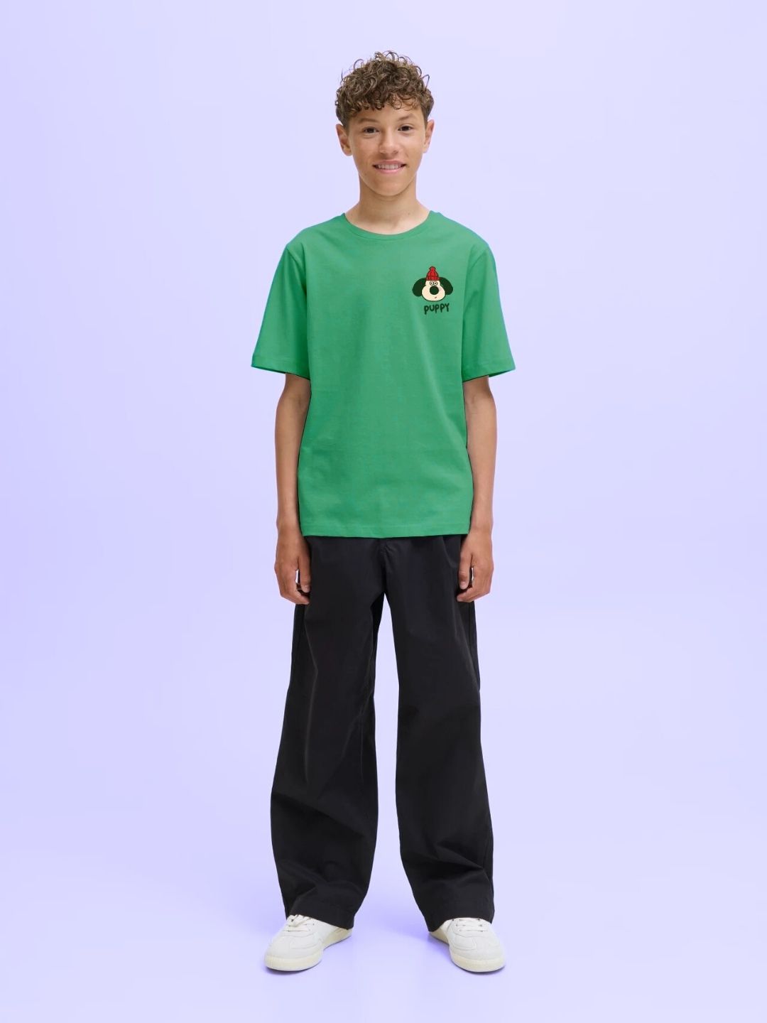 Boy wearing a TADDY PUPPY T-SHIRT FOR BOYS AND GIRLS GREEN with black pants and sneakers, front view.