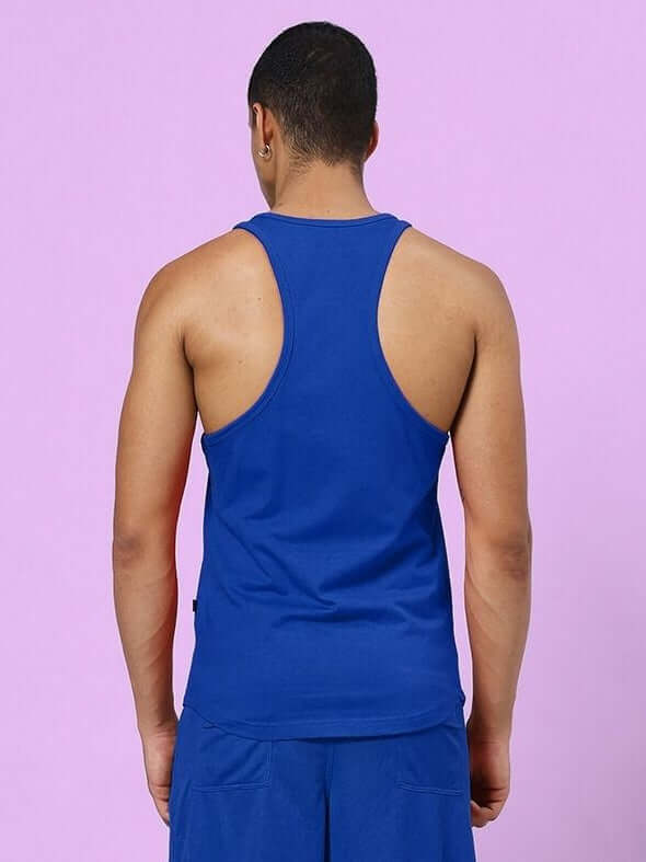 Back view of model wearing TAKE IT EASY GYM VEST T-SHIRT BLUE against purple background, showcasing sporty design for fitness and leisure.