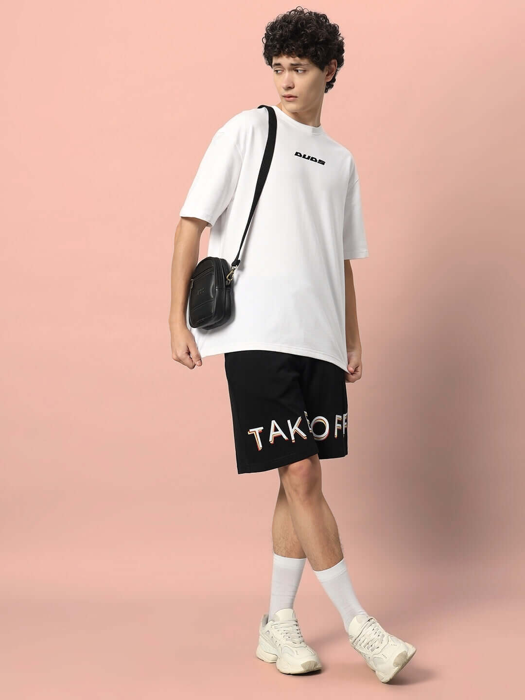 Model wearing black TAKE OFF regular fit shorts with white t-shirt and sneakers, showcasing casual style and customizable fit options.