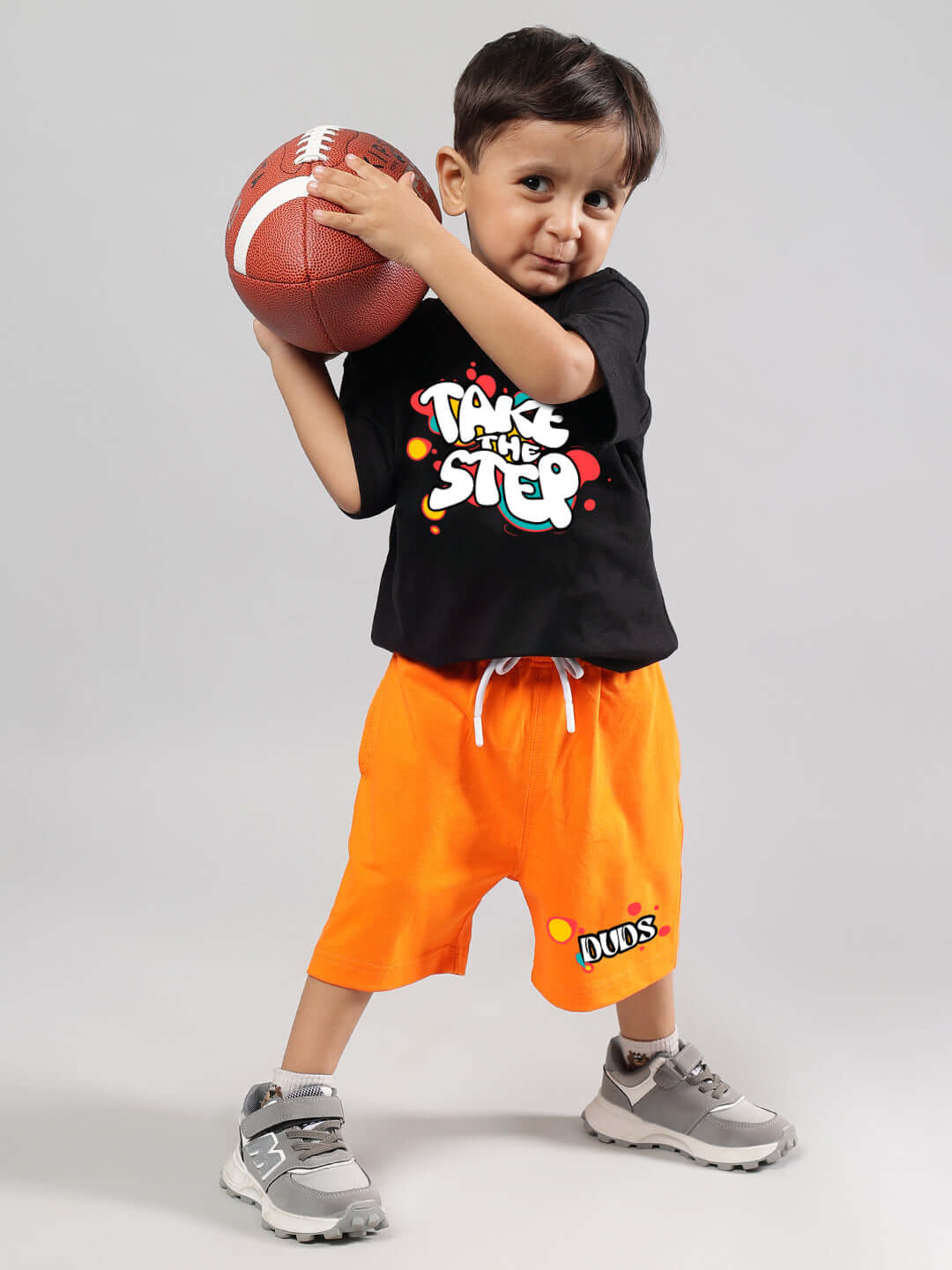 Child wearing TAKE THE STEP CO-ORD FOR BOYS GIRLS BLACK-ORANGE outfit holding a football, showcasing vibrant streetwear style.