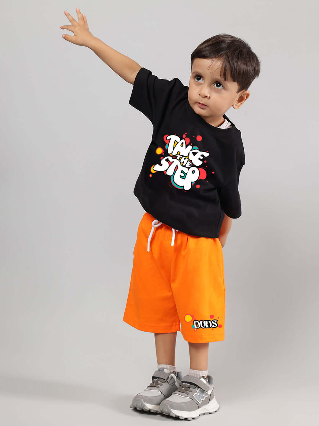 Child wearing TAKE THE STEP CO-ORD FOR BOYS GIRLS BLACK-ORANGE, featuring a black top with graphic design and orange shorts.