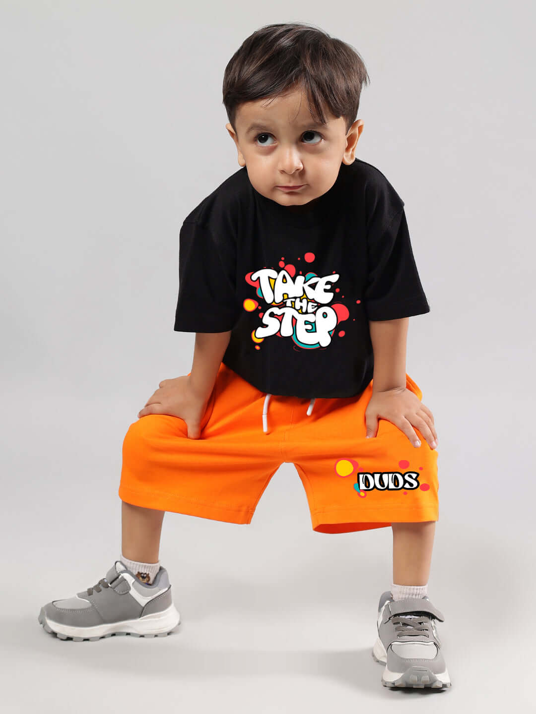 Child wearing orange "Take the Step" shorts by DUDS, with a playful pose.