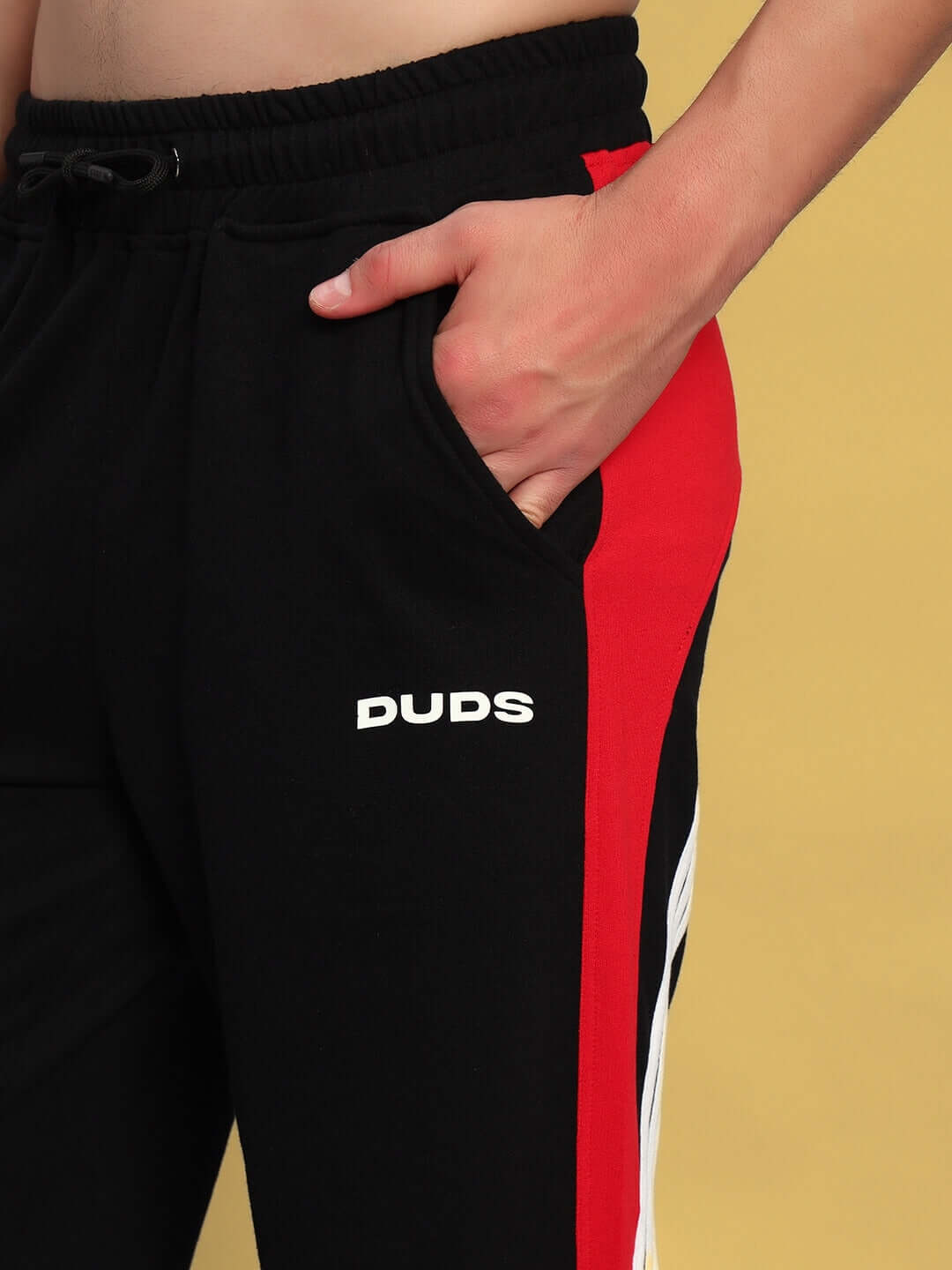 Man wearing TANGLE Relaxed-Fit Joggers in black-red by DUDS, showcasing side stripe design and logo detail.