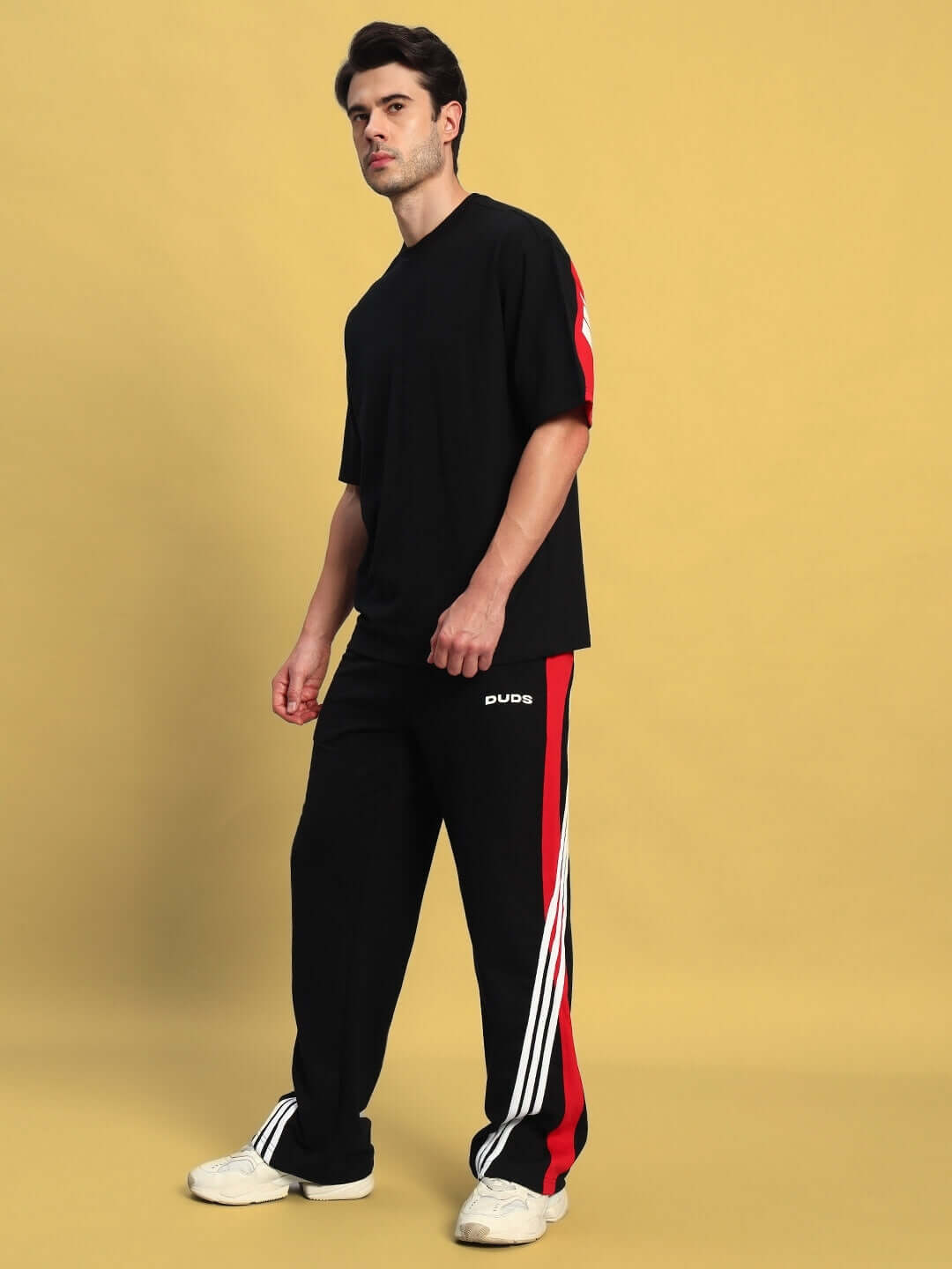 Man wearing TANGLE Relaxed-Fit Joggers in black and red by DUDS, standing against a yellow background.