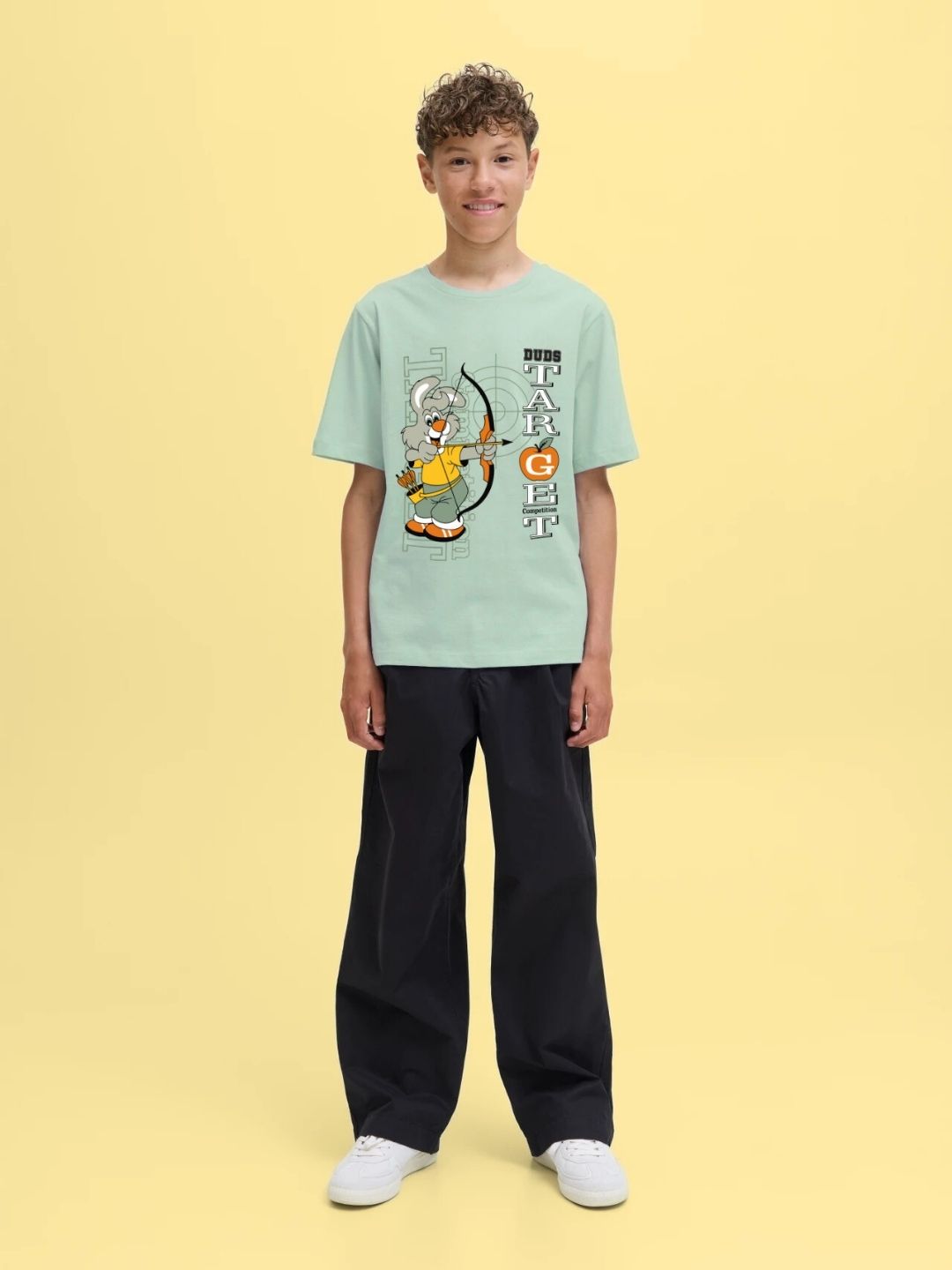 Boy wearing TARGET PRINTED T-SHIRT FOR BOYS AND GIRLS LIGHT GREEN with bold target print, styled with black pants and white sneakers.