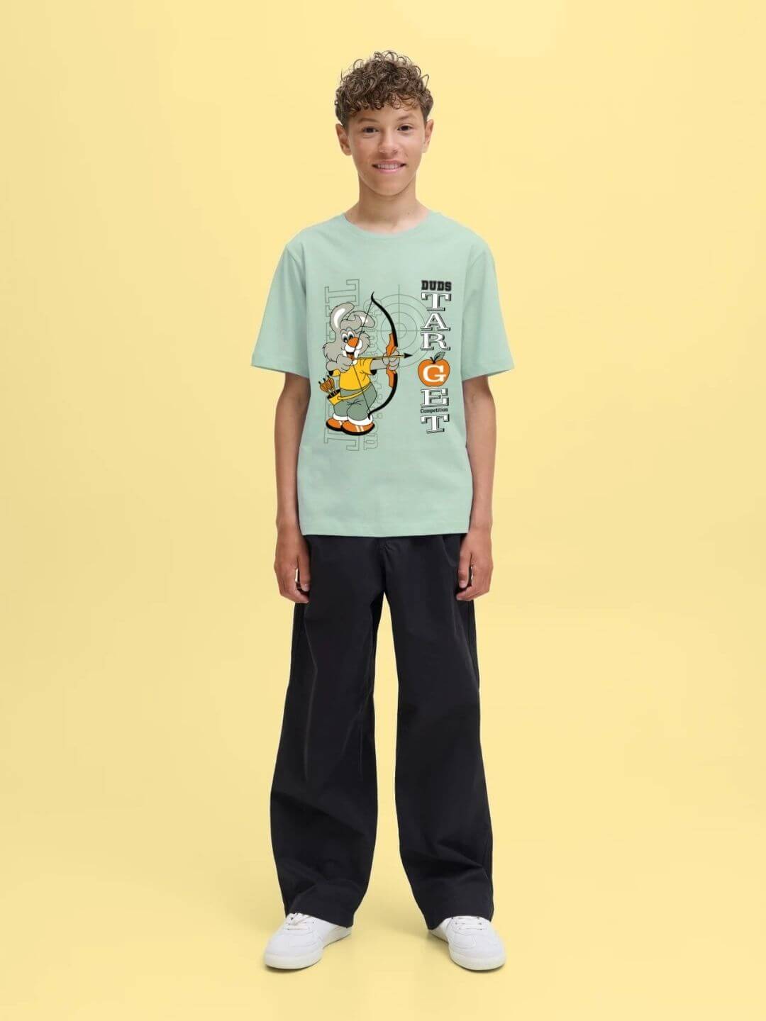 Boy wearing TARGET PRINTED T-SHIRT FOR BOYS AND GIRLS LIGHT GREEN with target-inspired print, standing on yellow background.