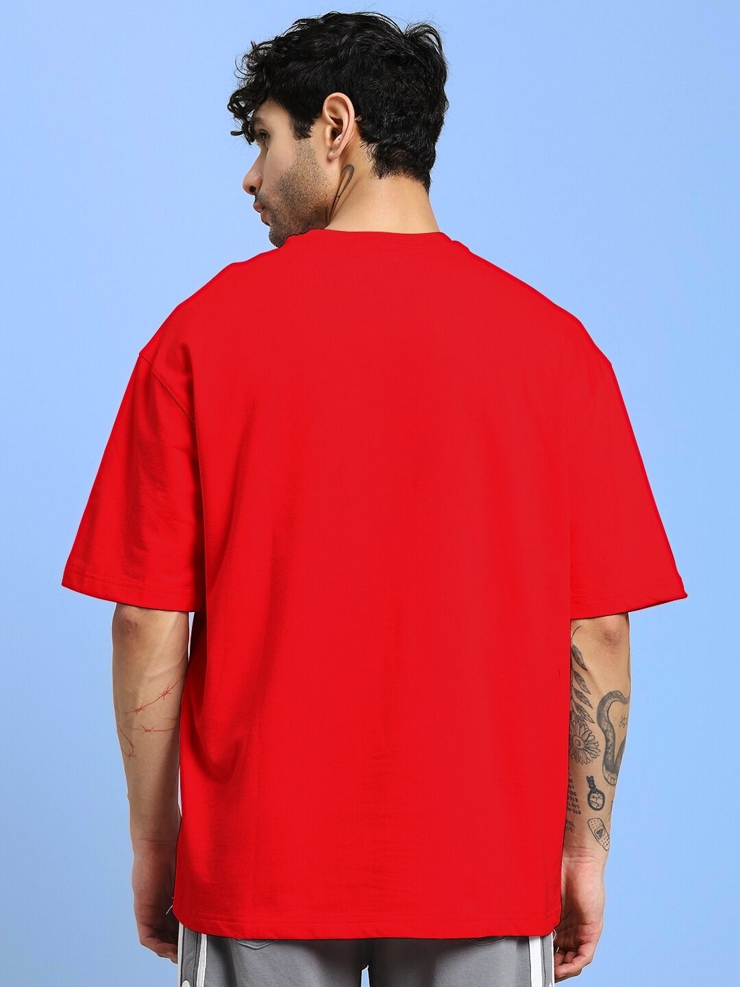 Back view of a model wearing TEKKEN KING T3 OVER-SIZED T-SHIRT RED with tattooed arm, illustrating fit and style.