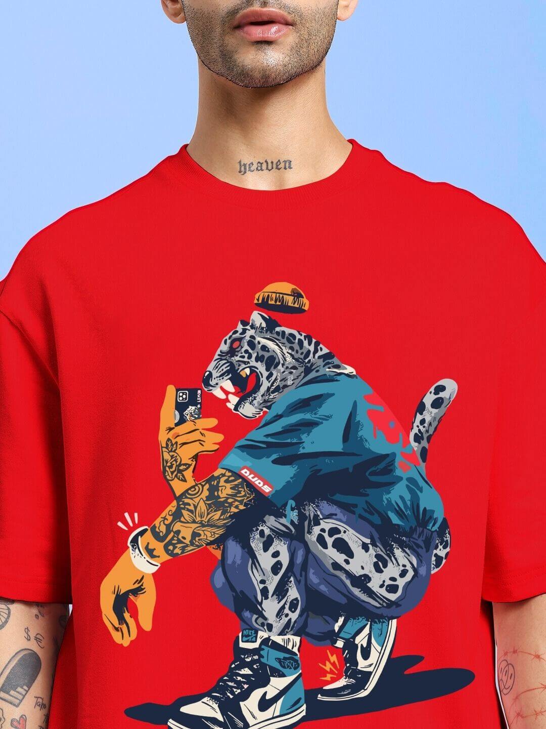 Person wearing TEKKEN KING T3 OVER-SIZED T-SHIRT RED with colorful graphic design and tattoos, showcasing bold streetwear style