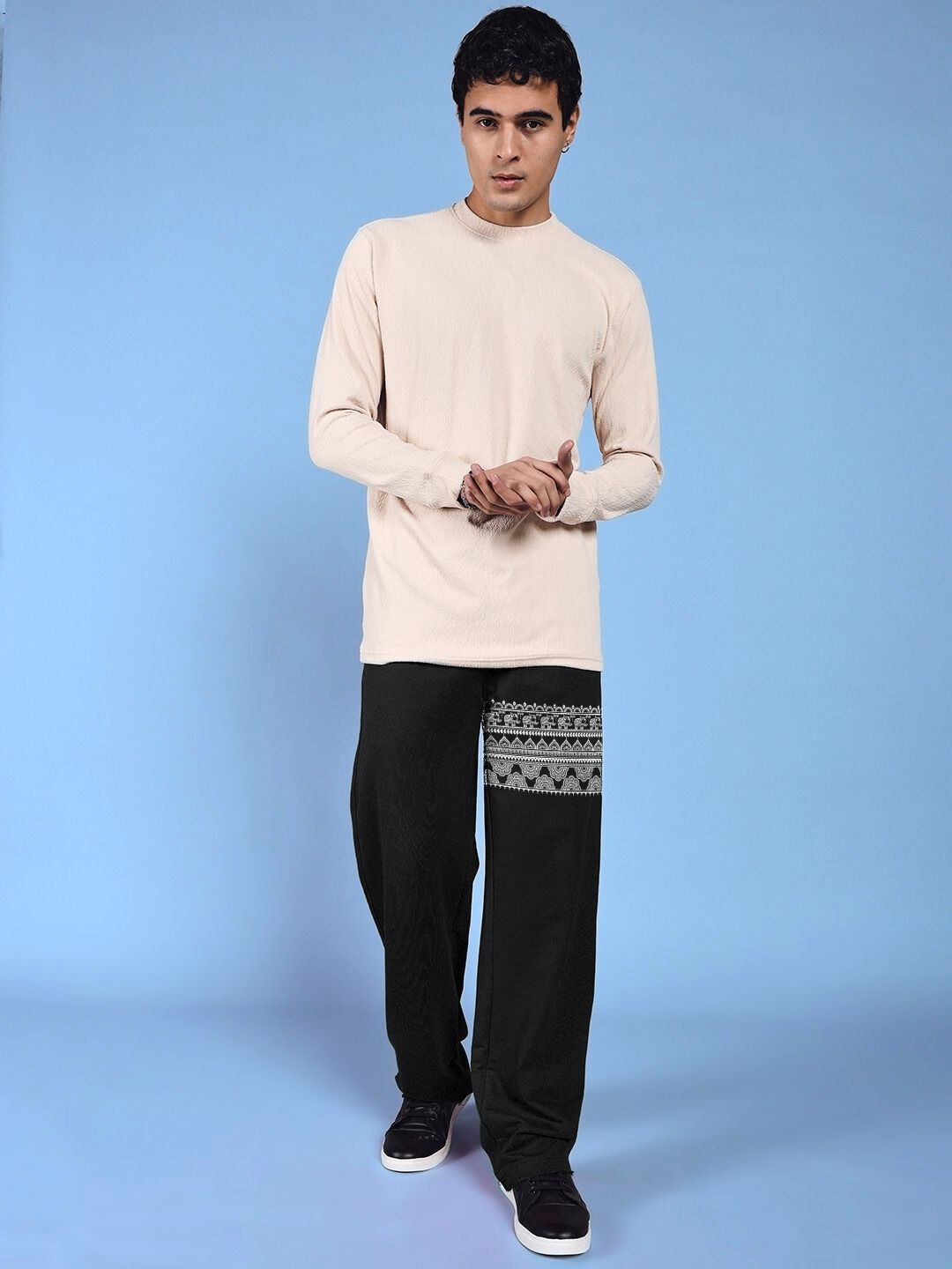 Model wearing THAI TRADITIONAL PRINTED RELAXED FIT JOGGER BLACK showcasing cultural artistry and modern street style against a blue backdrop.