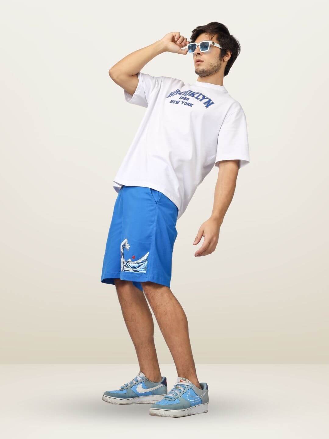 Model wearing The Great Wave regular fit shorts in blue with wave design, offering custom fit option, styled with casual sneakers.