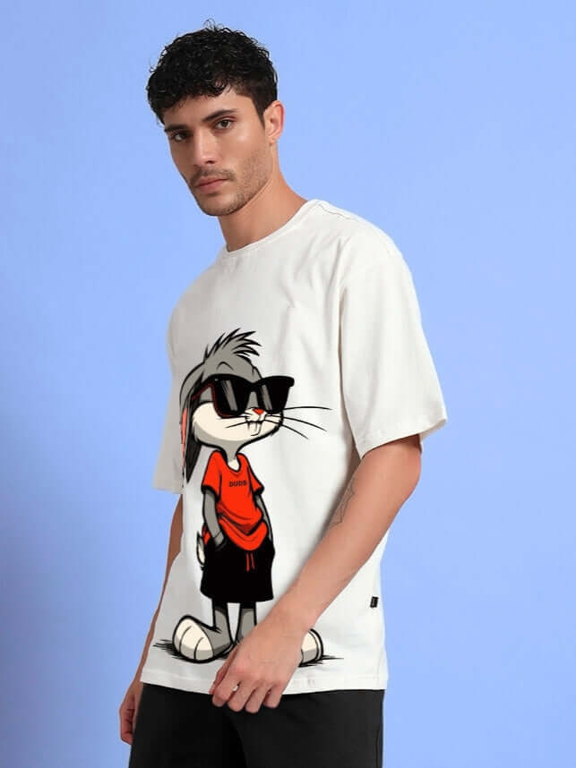 Model wearing THINK BIG BUNNY TOONS OVERSIZED T-SHIRT OFF WHITE with graphic print on a blue background.