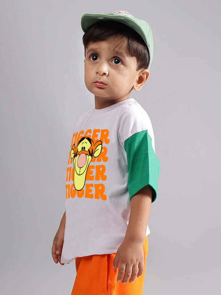 Child wearing a white oversized T-shirt with a tiger print, featuring green sleeves and an orange cap.