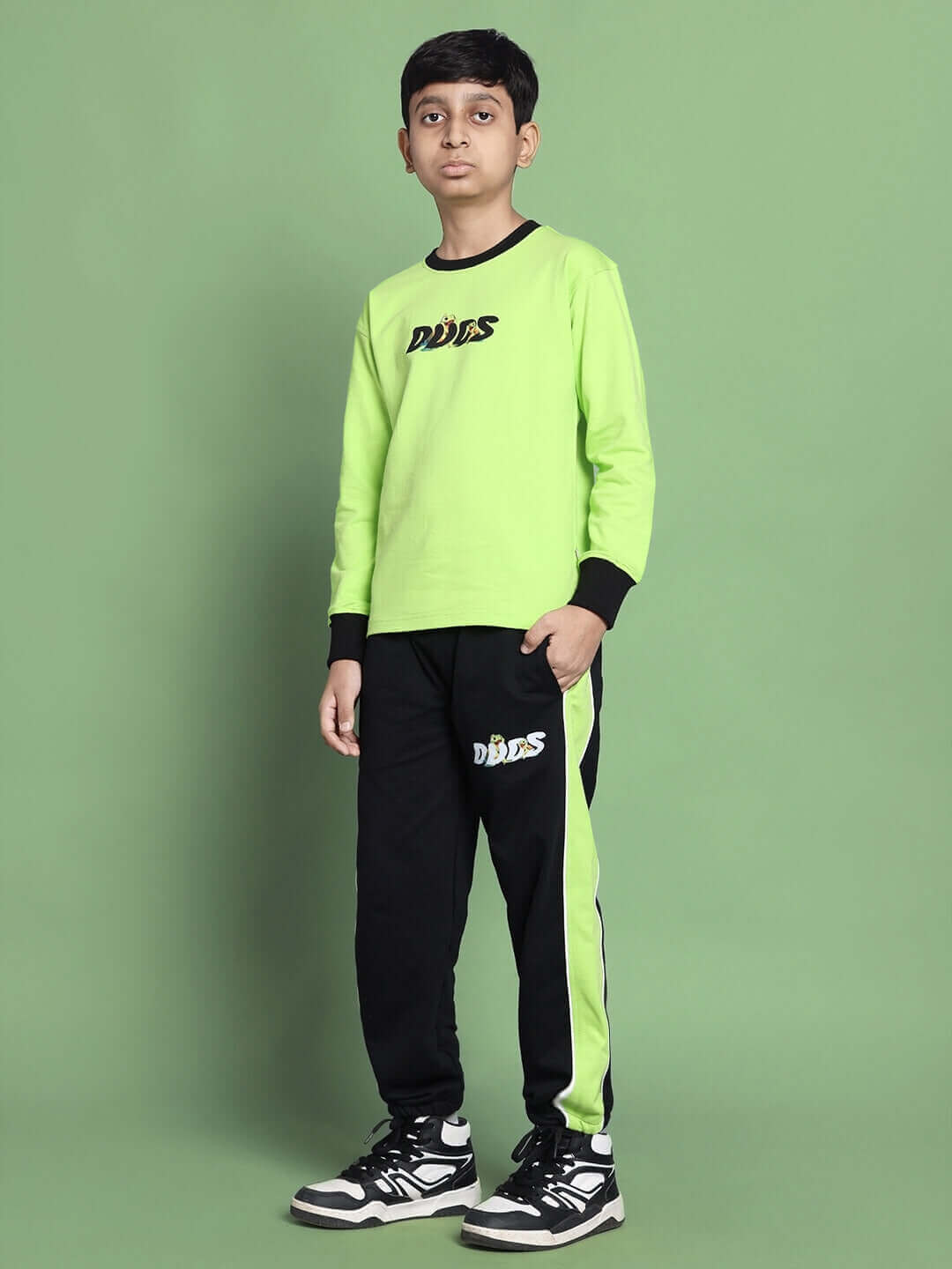 Child wearing TILLY oversized neon green sweatshirt for boys and girls, premium cotton, styled with black pants, standing on green background.