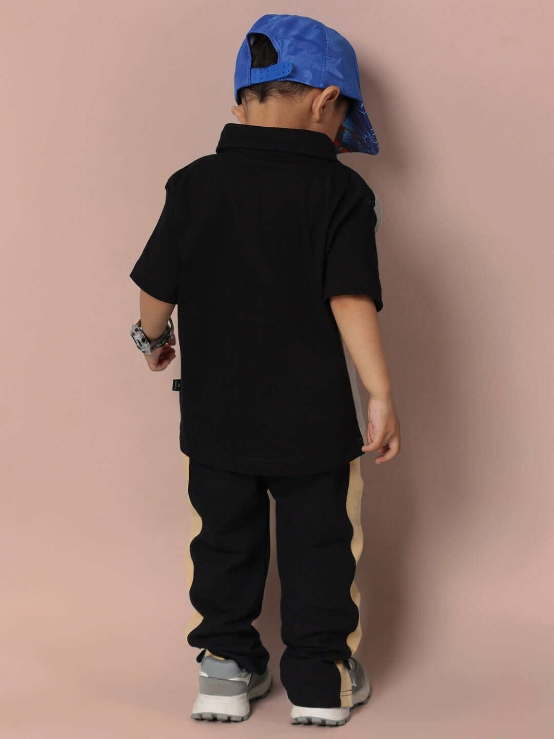 Child wearing TINGE CO-ORD FOR BOYS & GIRLS GREY BLACK in a fashionable pose with a blue cap and sneakers, facing away.