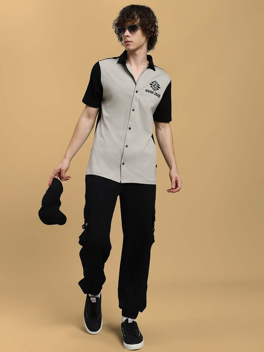 Model wearing Tinge regular fit grey-black shirt and black pants against beige background.