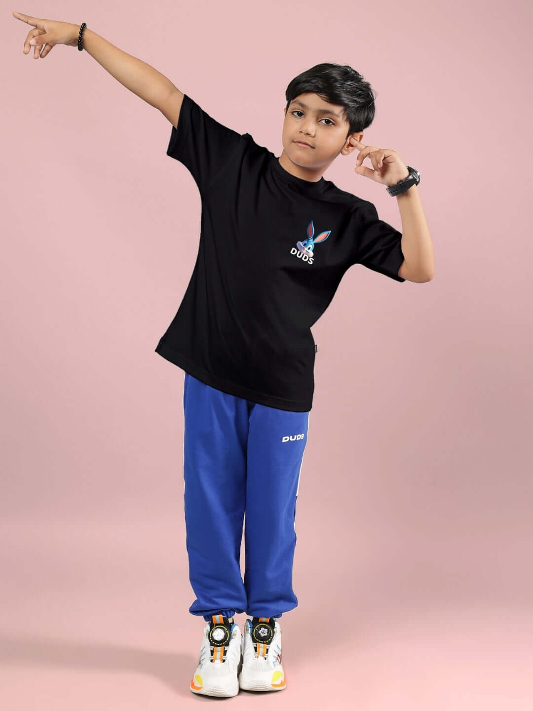 Boy wearing TINY TOON PRINTED CO-ORD FOR BOYS & GIRLS BLACK-R BLUE from DUDS, standing confidently against a pink background.