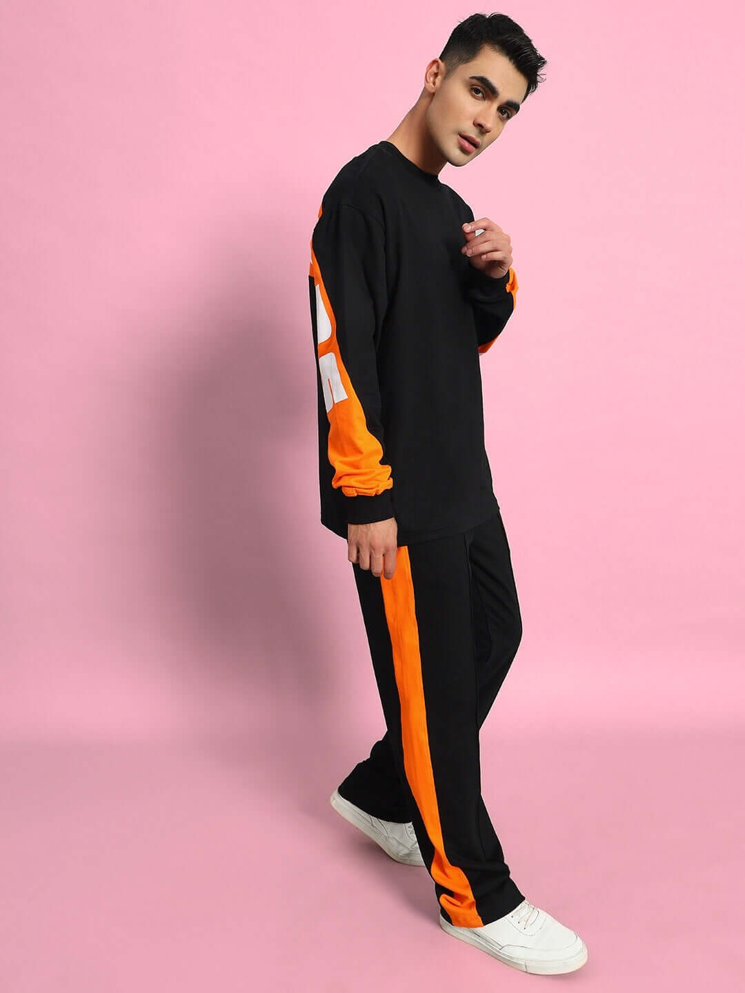 Model wearing TITAN oversized co-ord set in black with orange accents, relaxed fit joggers, and contrast panels, against a pink background.
