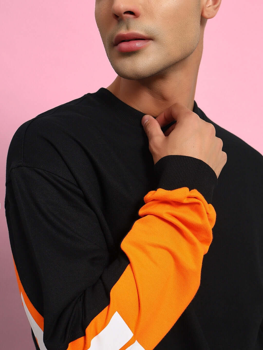 Person wearing a black and orange long-sleeve top, showcasing vibrant contrast sleeves against a pink background.