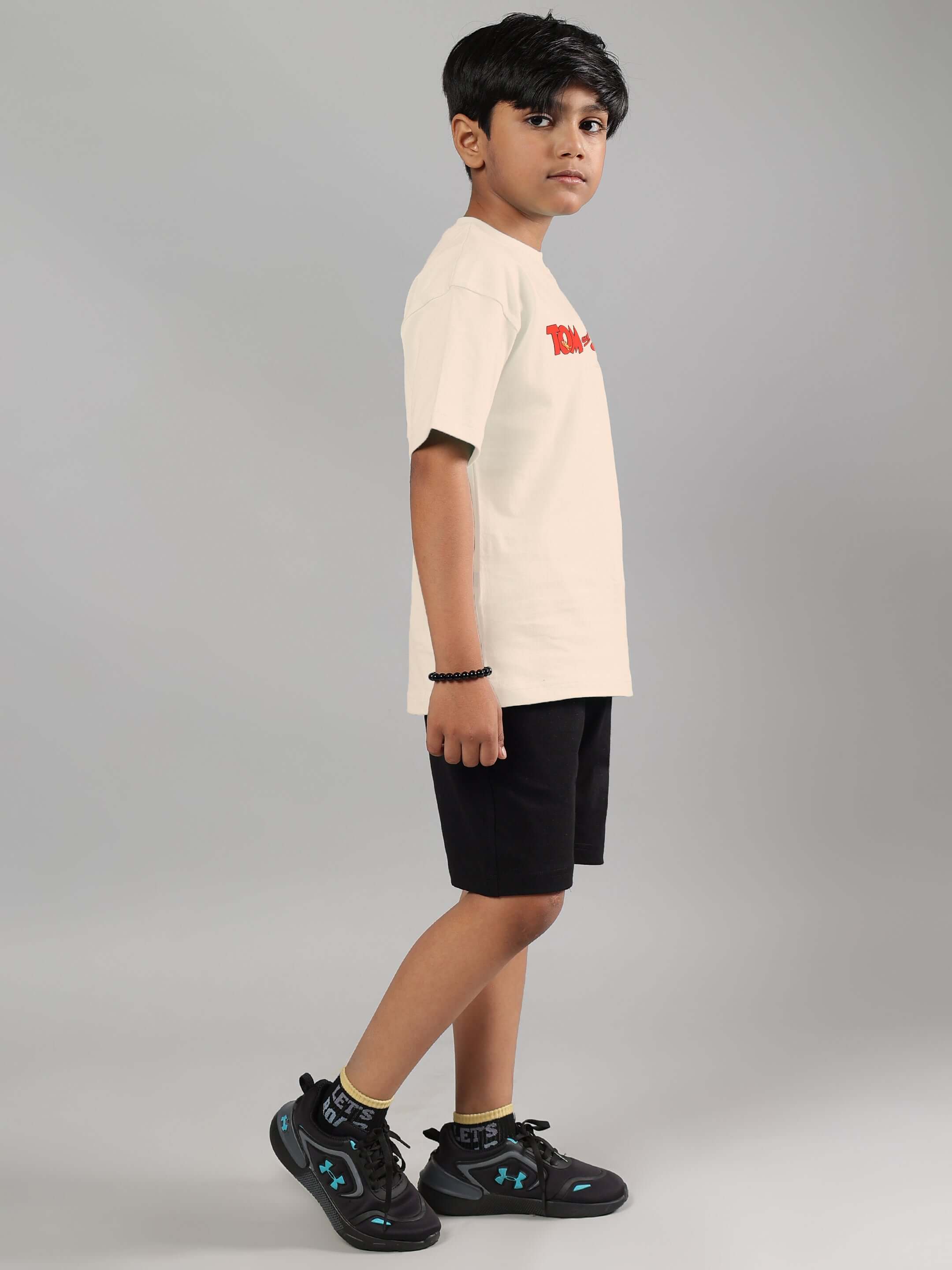 Boy wearing off-white and black Tom & Jerry co-ord set, side view with black shorts and sneakers. Made by DUDS, customizable fit.
