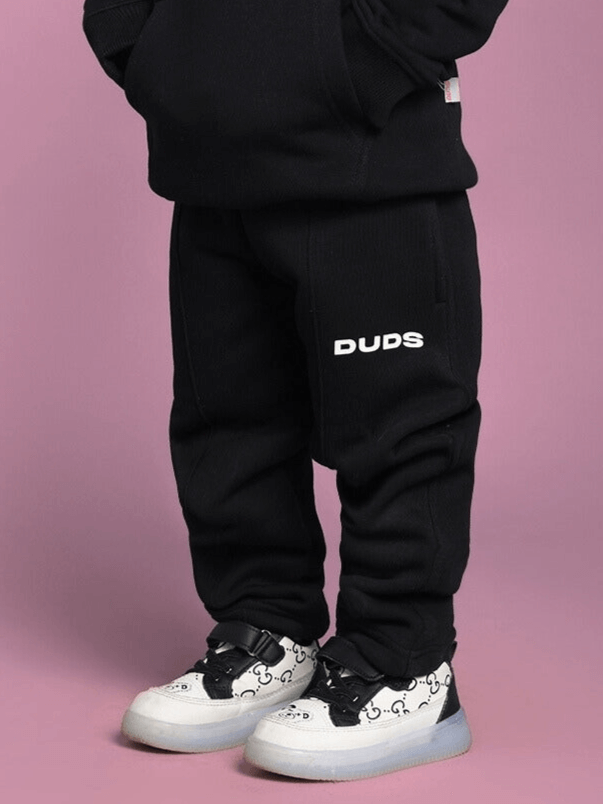 Child wearing TOM AND JERRY OVERSIZED FLEECE CO-ORD FOR BOYS GIRLS BLACK with colorful sneakers on pink background.