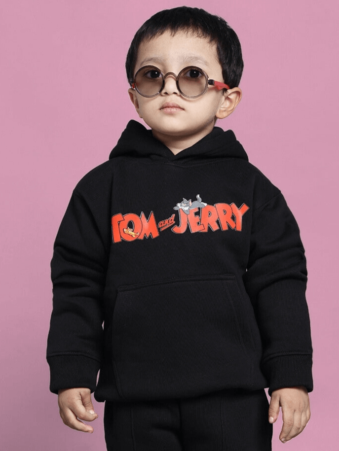 Child wearing black Tom and Jerry oversized hoodie for boys and girls, against a pink background.