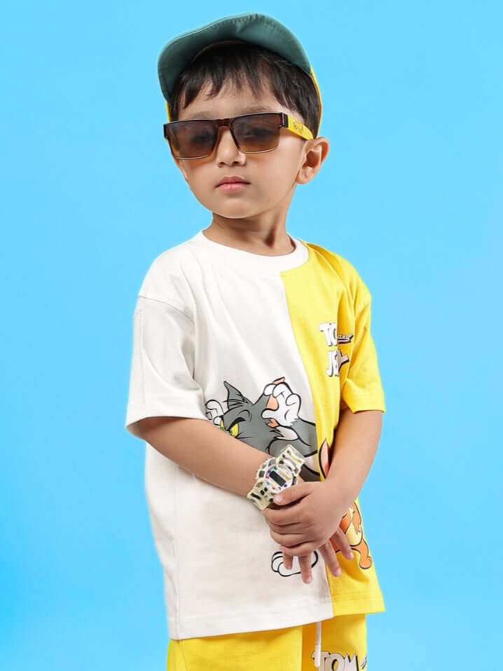 Young boy wearing Tom & Jerry oversized off-white-yellow t-shirt, sunglasses, and a cap, showcasing trendy casual kids' fashion.