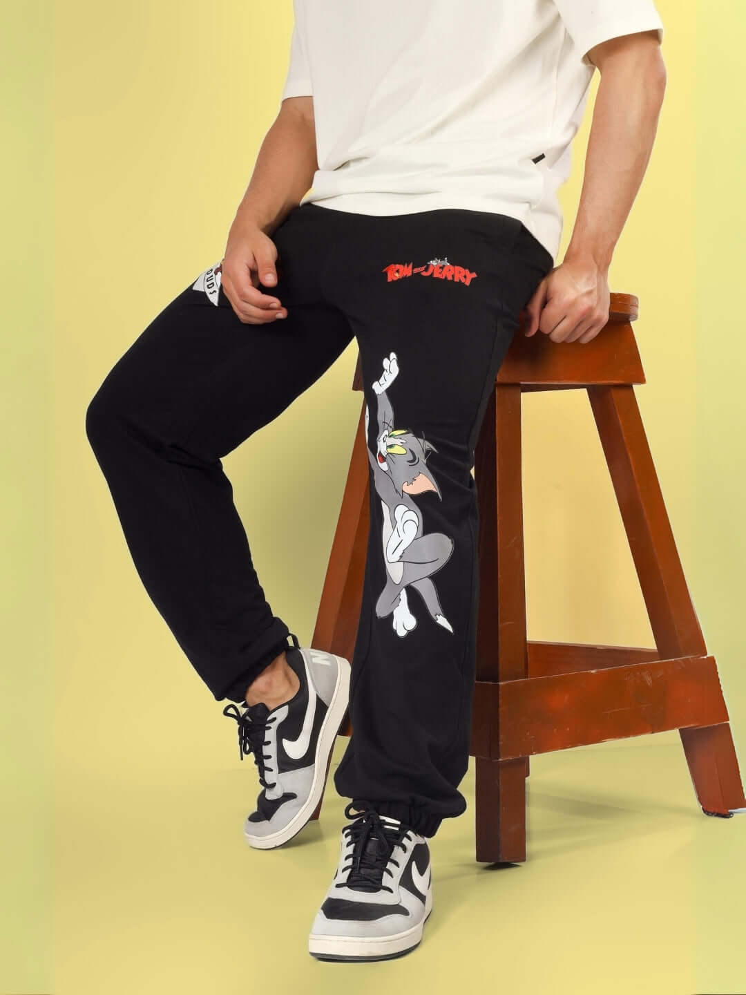 Person wearing Tom & Jerry relaxed black joggers with custom fit option by DUDS, displaying cartoon character design.