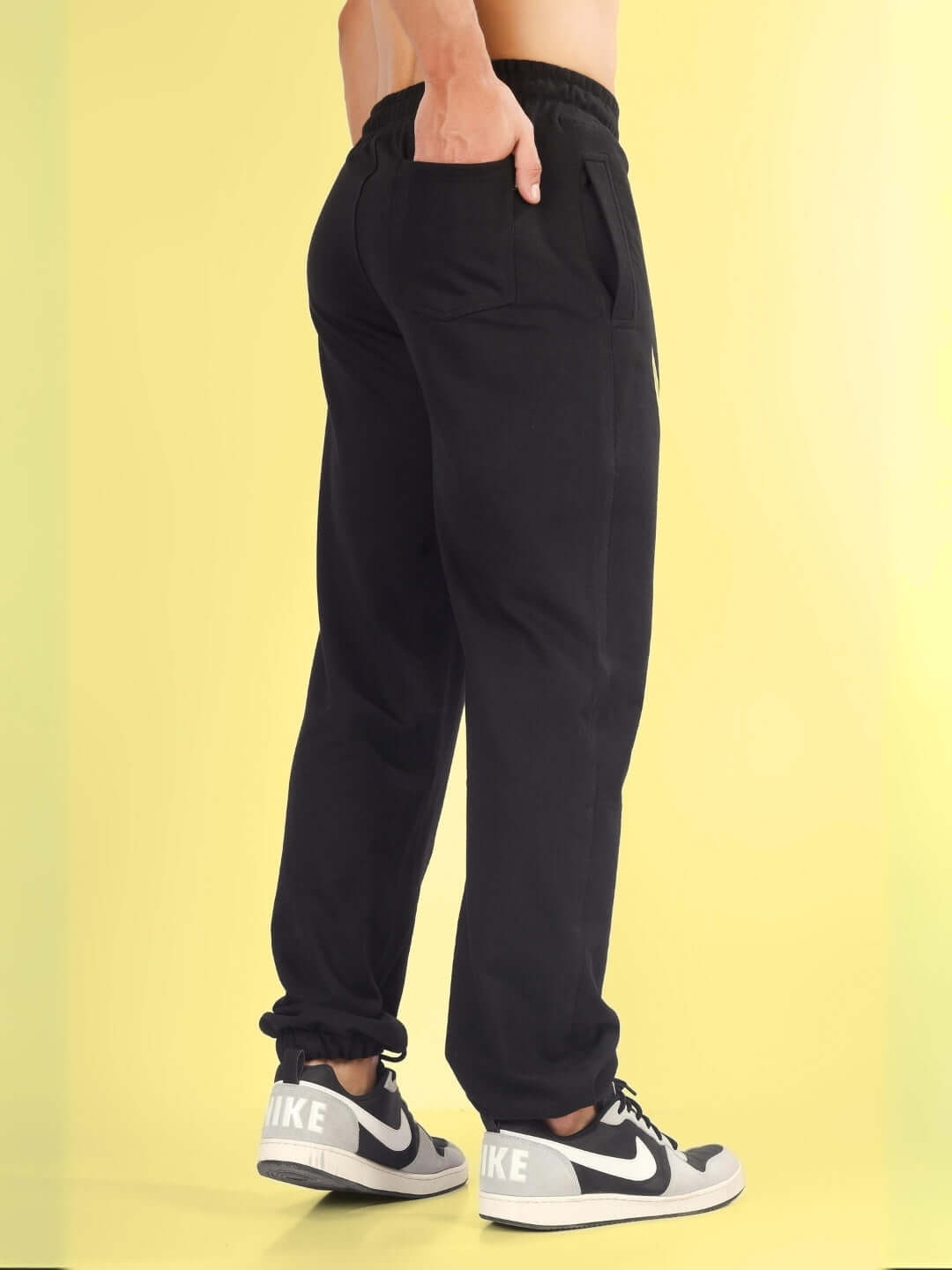 Person wearing TOM & JERRY Relaxed Jogger in black, showcasing back pocket detail, with yellow background.