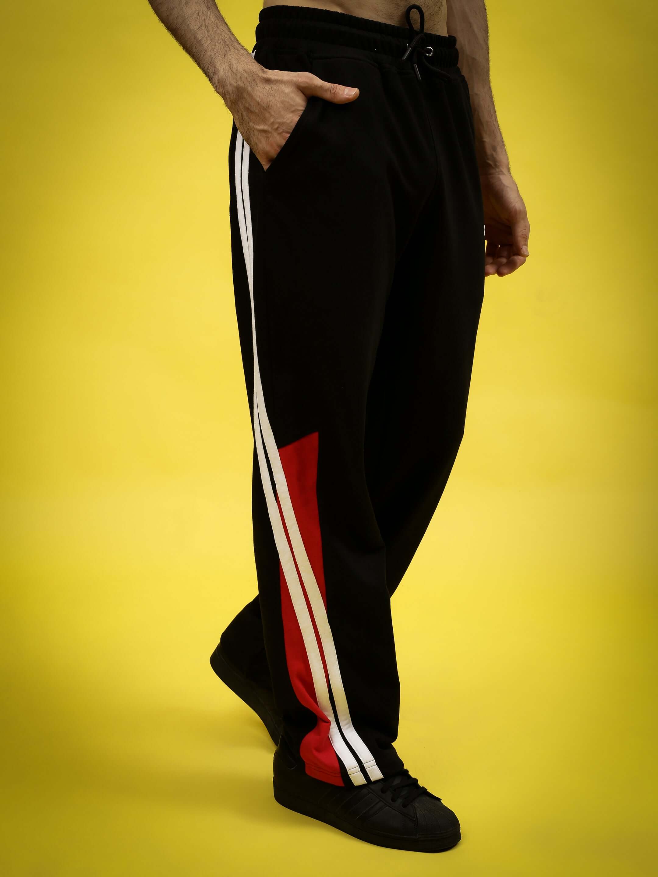 Man wearing Tornado Joggers in Black Red with stripe detail, showcasing a sporty design against a yellow backdrop, by DUDS.