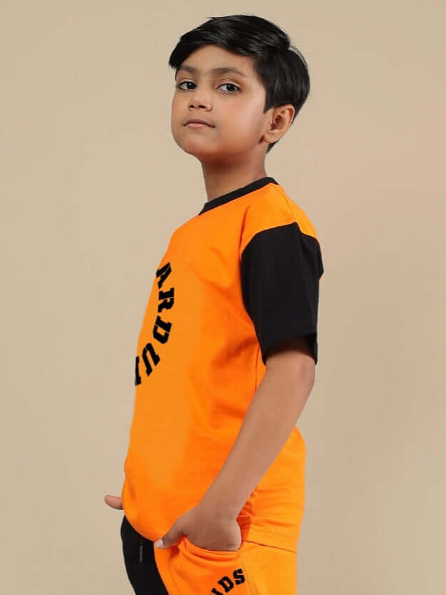TRACK & FIELD T-SHIRT FOR BOYS & GIRLS BLACK-ORANGE Boy wearing black and orange Track & Field t-shirt from DUDS, designed for both boys and girls, side view showcasing the design.