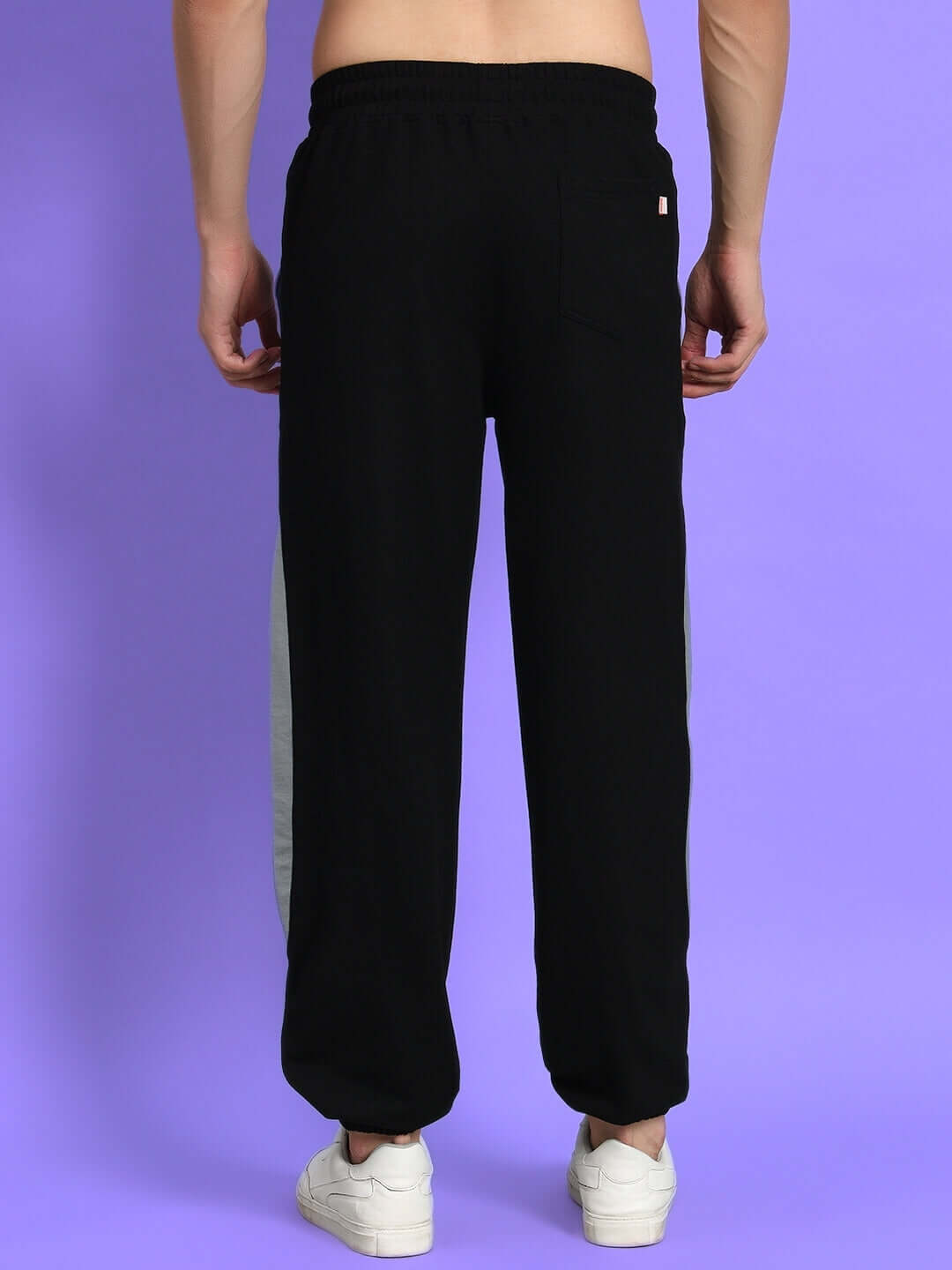 Back view of Trackpoint Baggy Joggers in black-grey, worn by model, showcasing design details on a purple background.