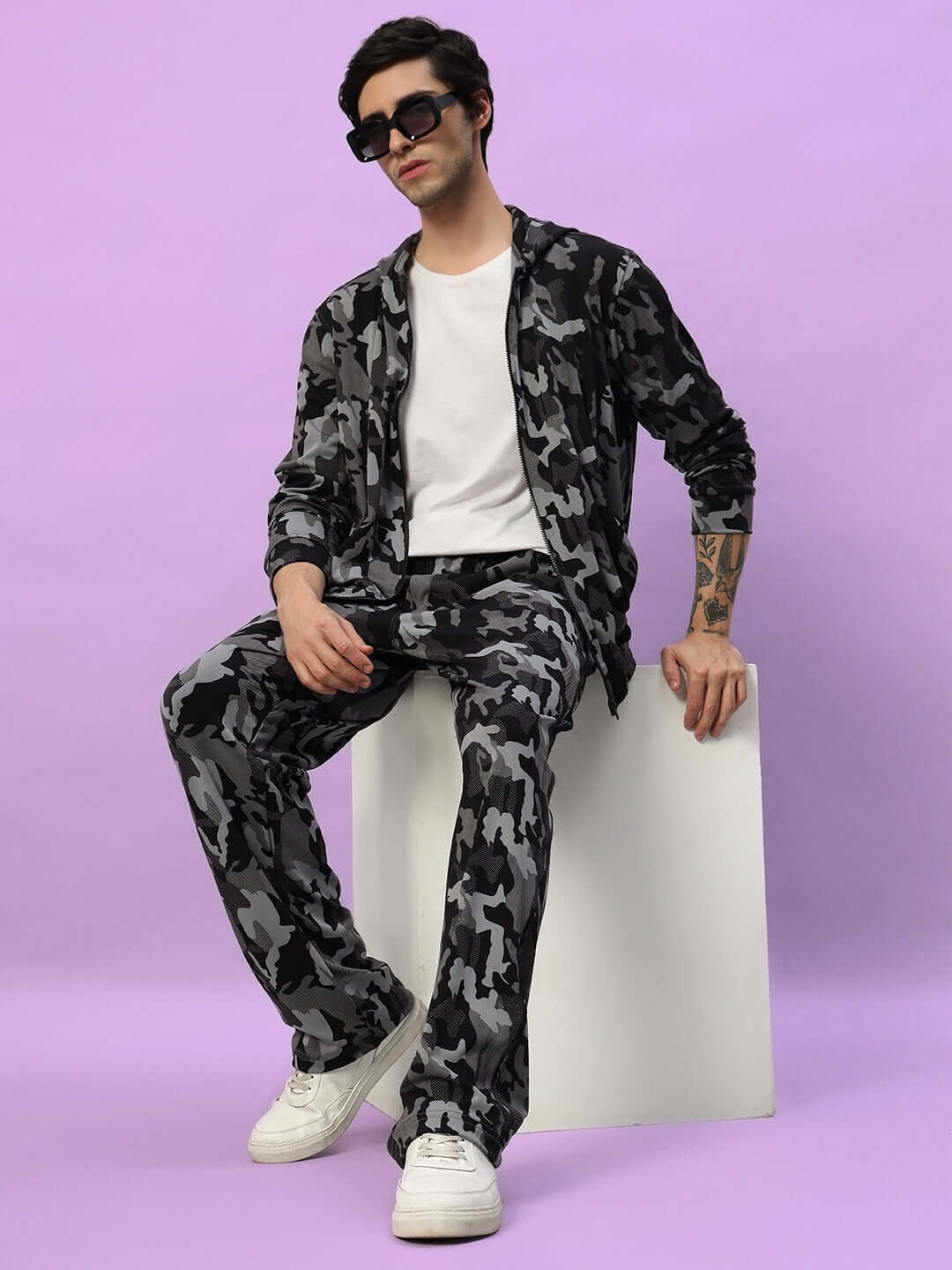 Model wearing DUDS Trench Relaxed Pant Jogger in Camo Navy with a casual white t-shirt, sitting against a purple background.