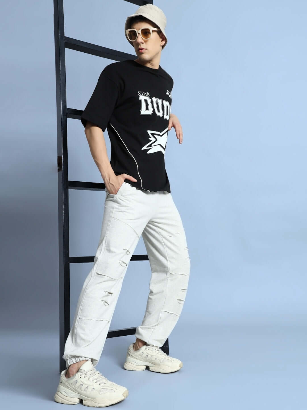 Male model wearing Duds Graze Joggers in Melange Grey, standing with casual pose, sunglasses, and white sneakers, against blue background.