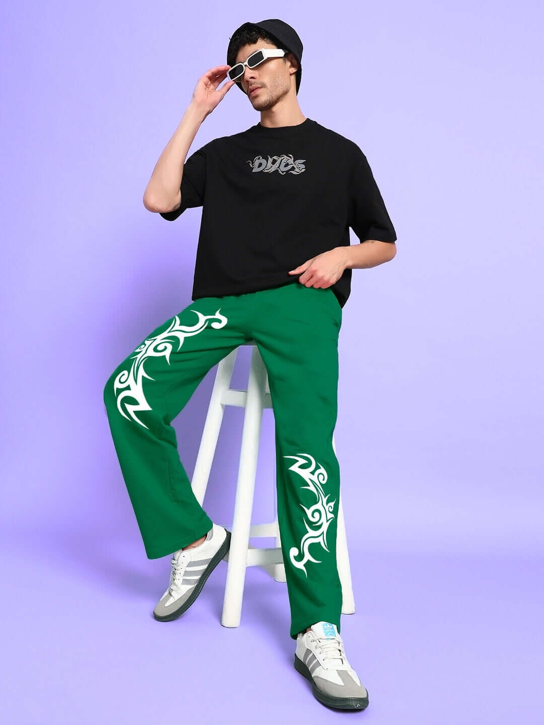 Model wearing TRIBAL STRONG SENSE JOGGER GREEN with streetwear style, sitting on a stool against a pastel background.