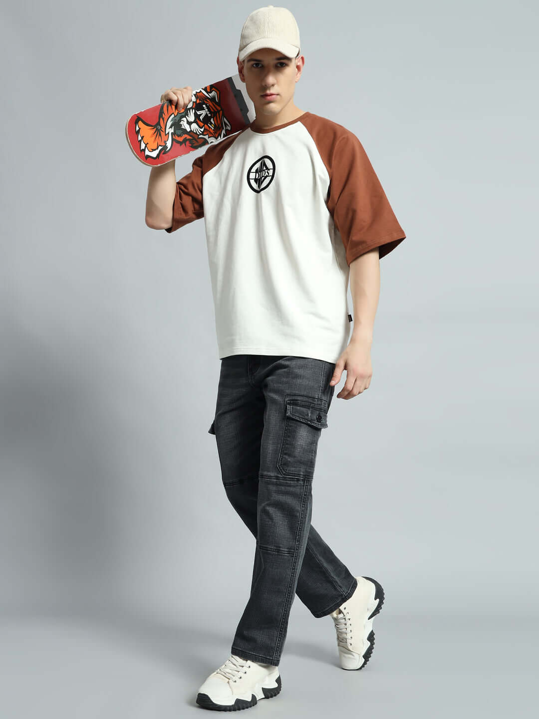 Model wearing TYRO Relaxed Denim Cargo in grey paired with a casual white and brown baseball tee, holding a skateboard.