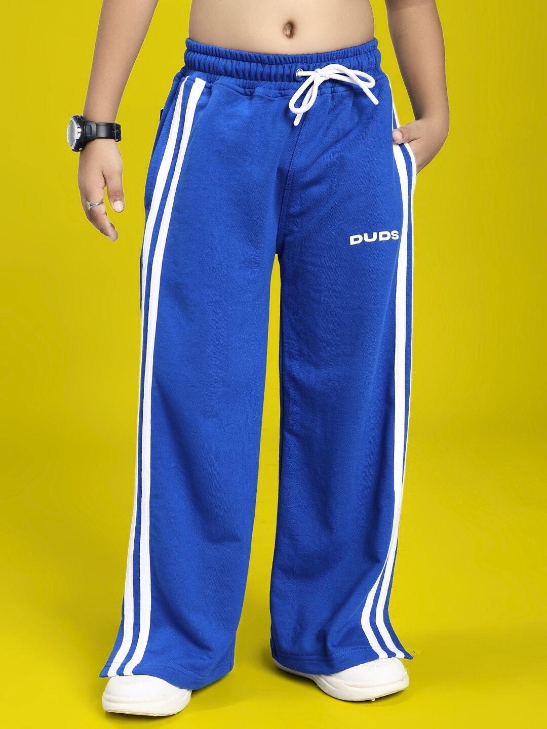 Child wearing UNITED STRIPE JOGGER FOR BOYS AND GIRLS BLUE with white sneakers on a yellow background.