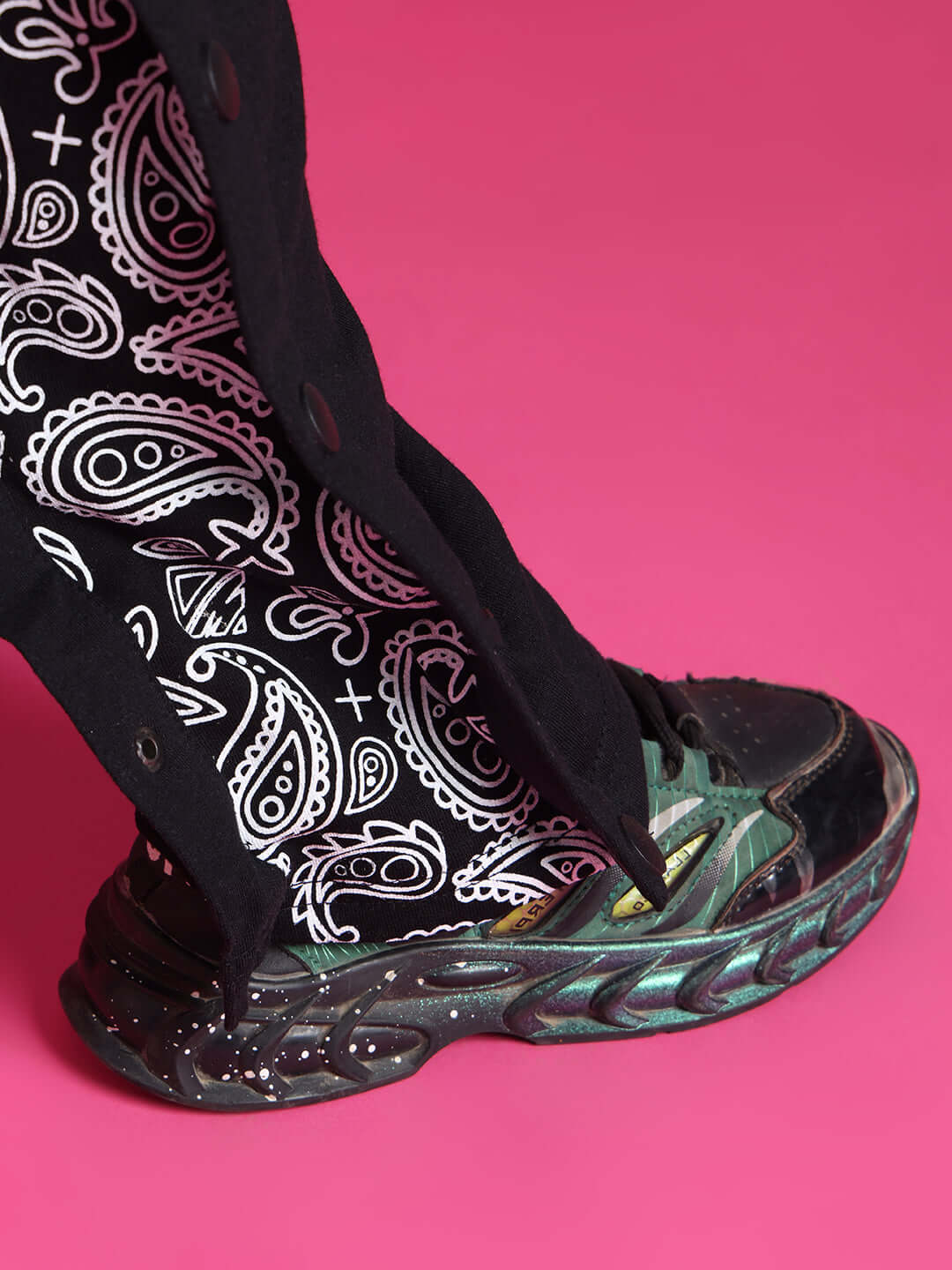 Close-up of a black motif co-ord with white paisley patterns and sneakers, set against a vibrant pink background.