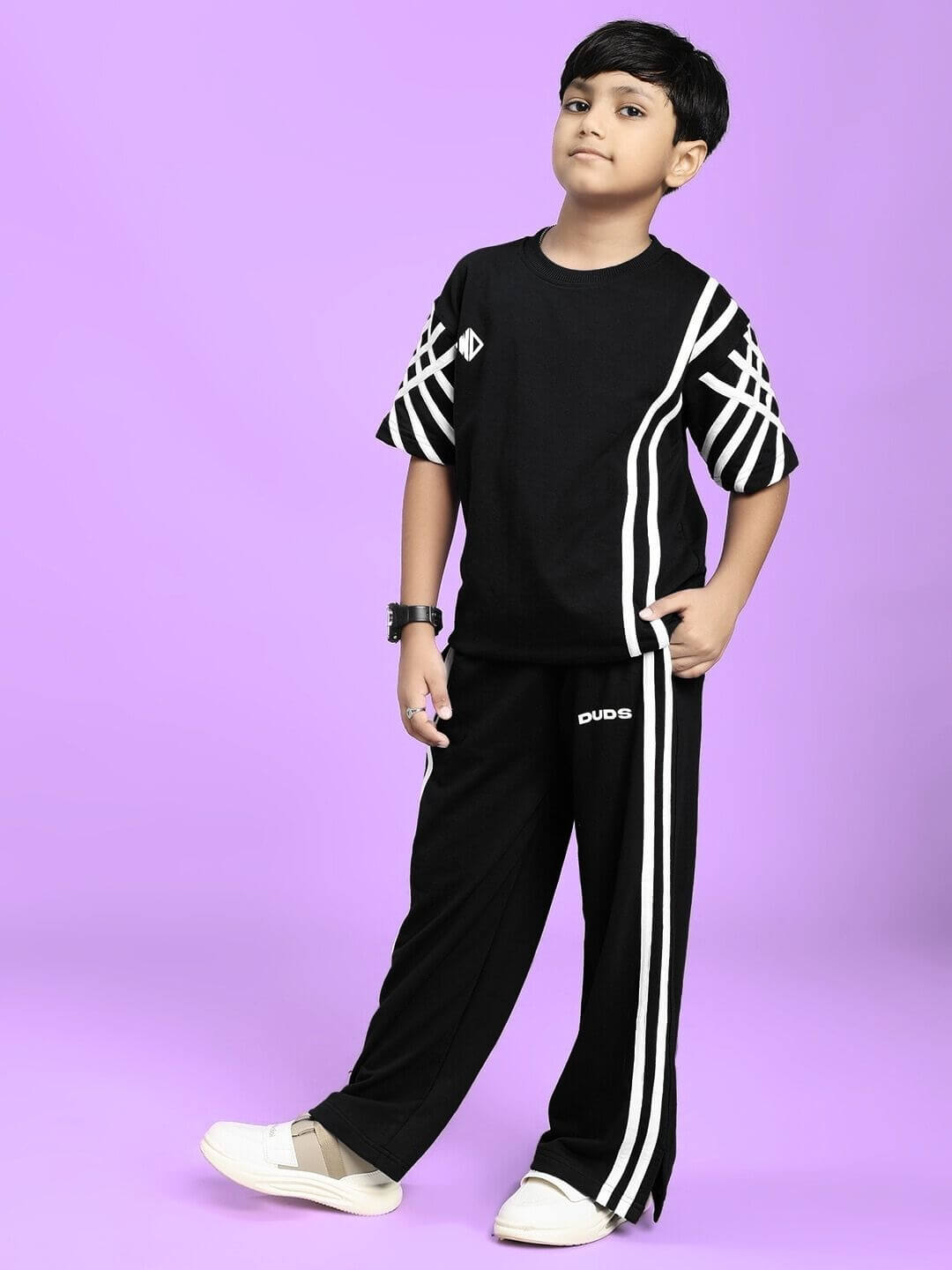 Child wearing UNITED STRIPE CO-ORD SET FOR BOYS GIRLS BLACK with sporty stripes, standing against a purple background.