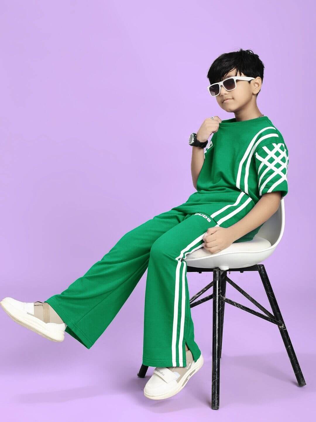 Boy wearing UNITED STRIPE CO-ORD SET FOR BOYS GIRLS GREEN with white stripes, sunglasses, seated on a chair against purple background