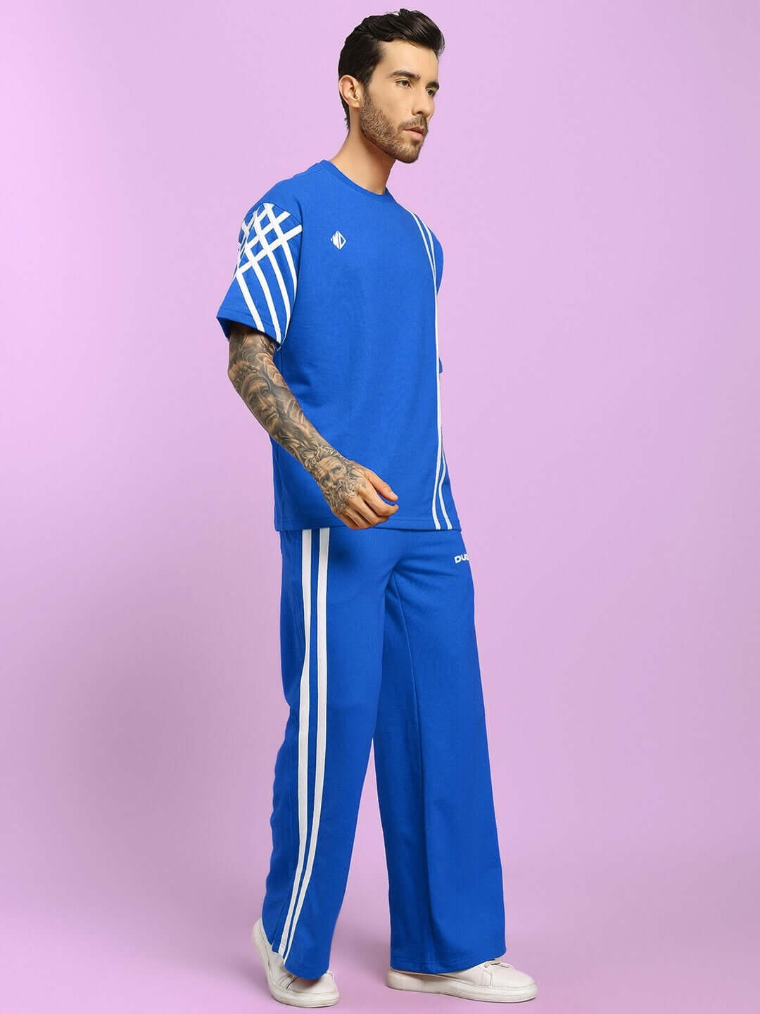 Man wearing UNITED STRIPE CO-ORD SET BLUE MEN with white stripe detailing, standing against a pink background in casual pose.
