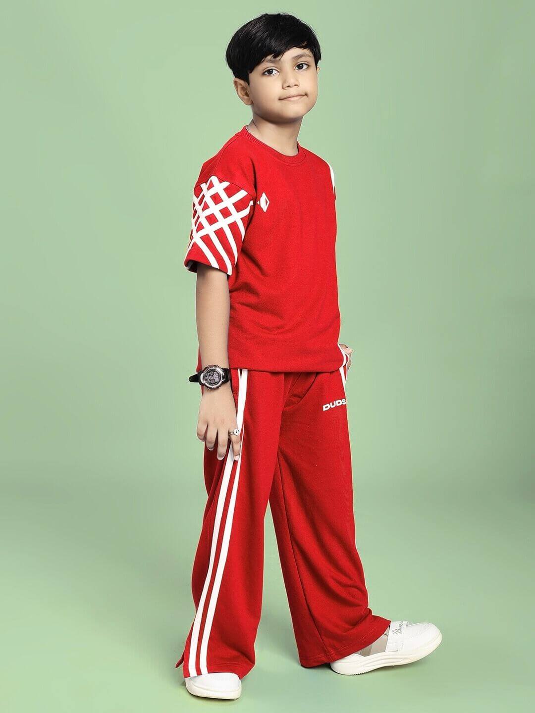 Boy wearing UNITED STRIPE CO-ORD SET FOR BOYS GIRLS RED with sporty white stripe accents and casual sneakers on a light green background.
