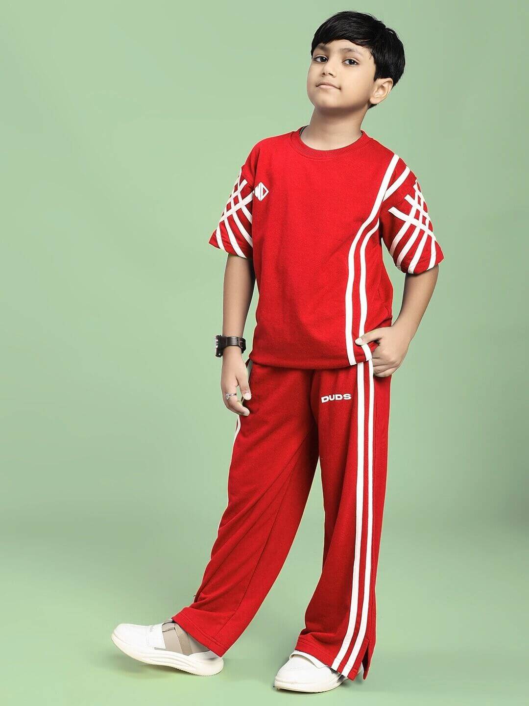 Child wearing UNITED STRIPE CO-ORD SET FOR BOYS GIRLS RED with sporty detailing and stripe accents, showcasing vibrant style on a green background.