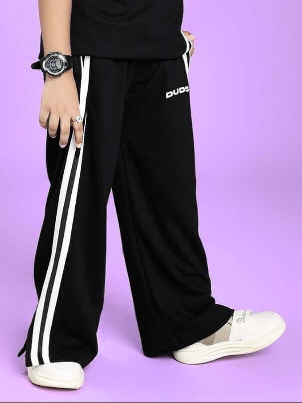 UNITED STRIPE JOGGER FOR BOYS AND GIRLS BLACK with white stripes, comfortable fit, shown with casual shoes on a purple background.