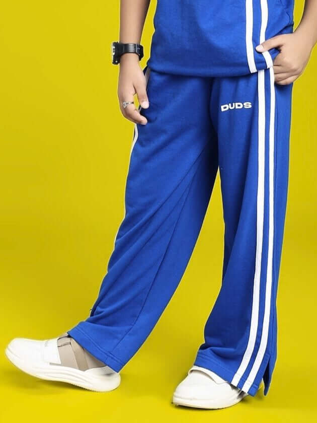 Child wearing blue UNITED STRIPE JOGGER FOR BOYS AND GIRLS BLUE with white stripes standing against yellow background.