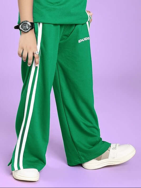 Child wearing UNITED STRIPE JOGGER FOR BOYS AND GIRLS GREEN with white stripes and sneakers on a purple background.