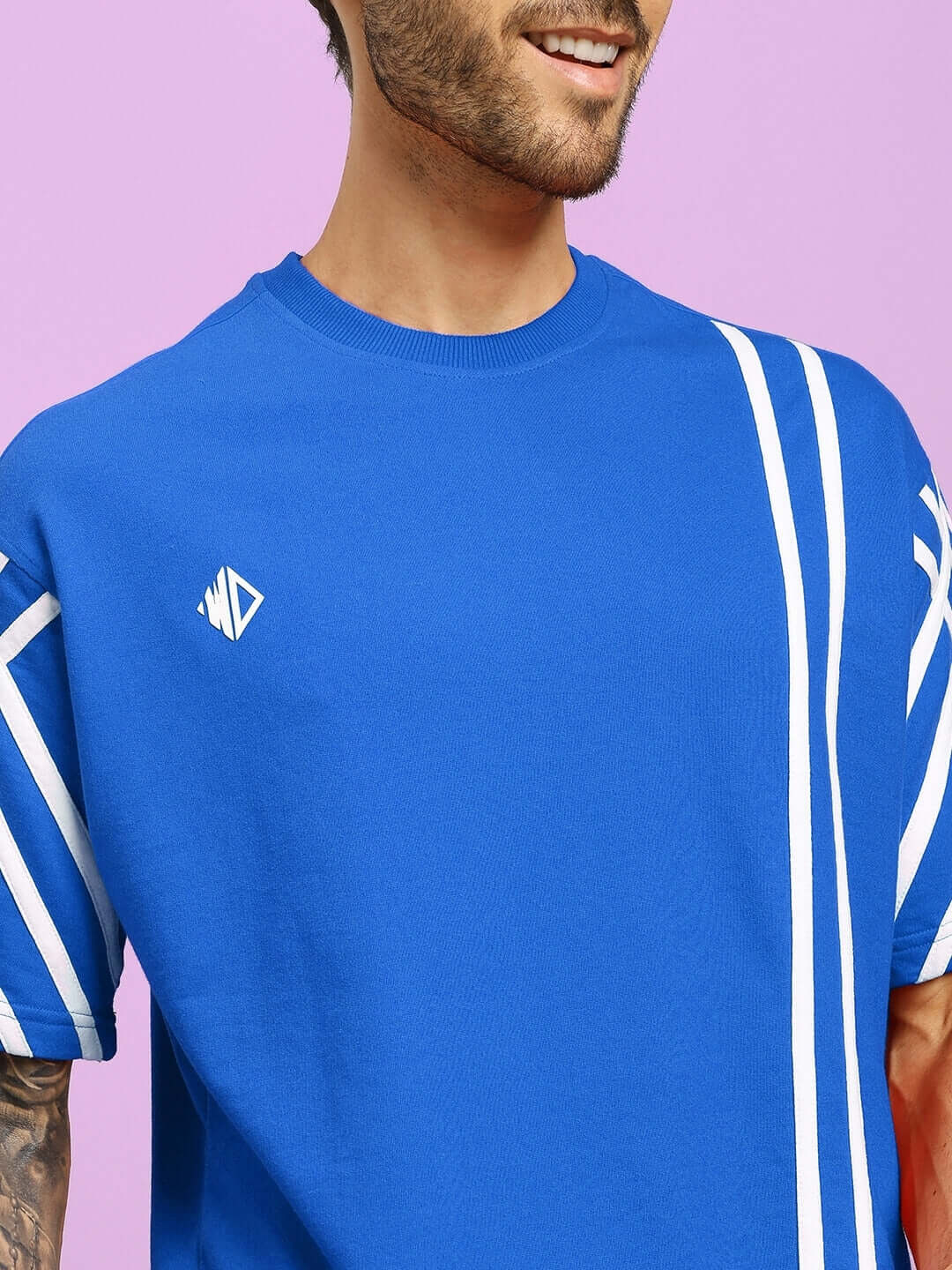 Model wearing UNITED STRIPE OVER-SIZED T-SHIRT in blue, made with premium cotton and elastane, featuring white stripes on a pastel background.
